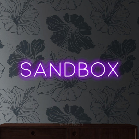 Purple LED neon sign reading "Sandbox" against grey floral wallpaper for gaming room décor