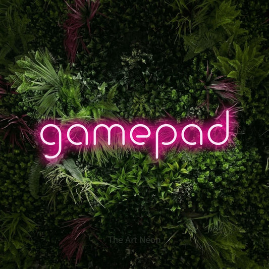 Hot pink LED neon sign reading "Gamepad" against a lush garden wall with pink flowers for gaming room décor