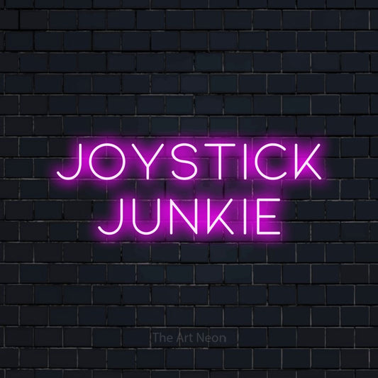 Pink LED neon sign reading "Joystick Junkie" against a dark navy brick wall for gaming room décor