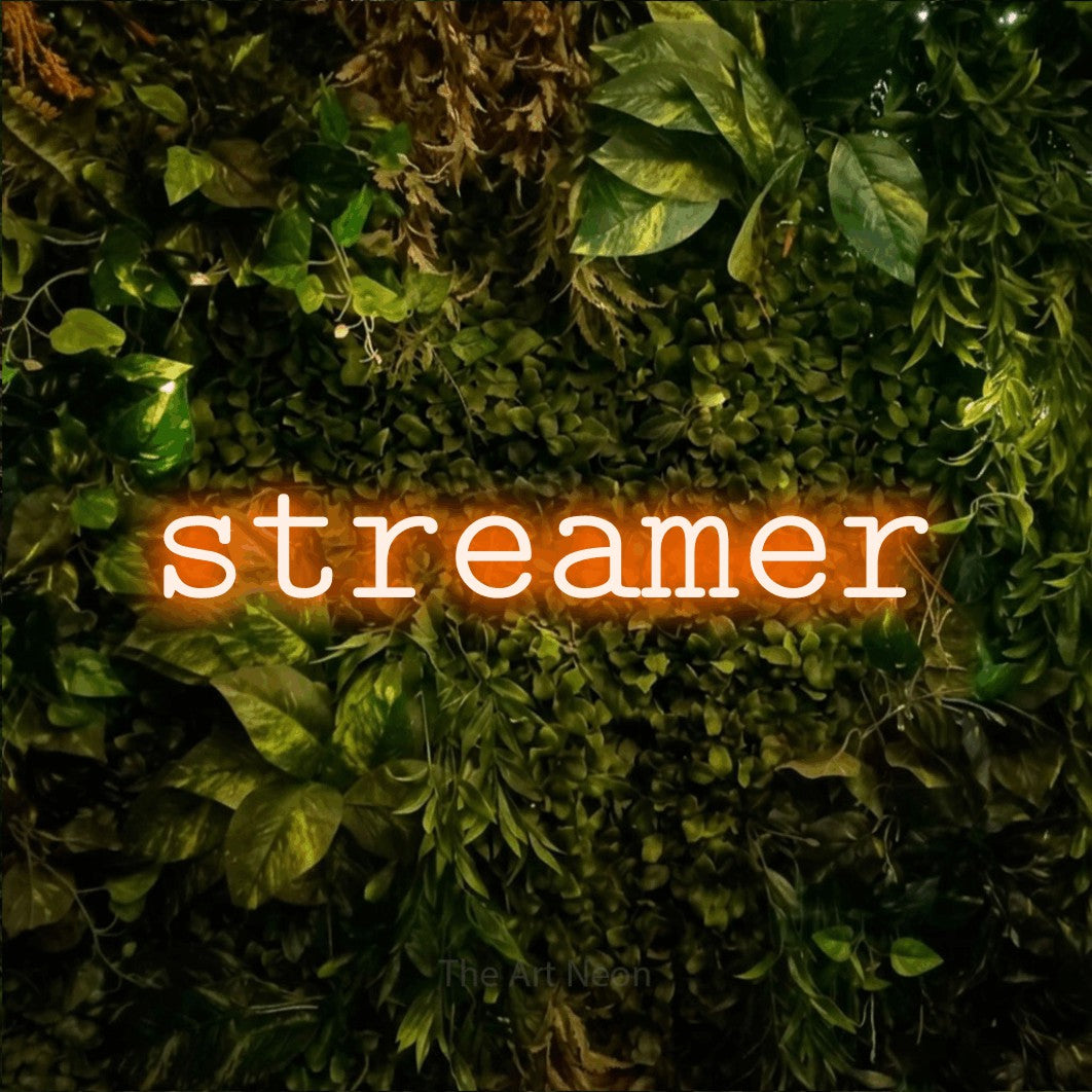 Orange LED neon sign reading "Streamer" against a textured moss and foliage wall for gaming room décor