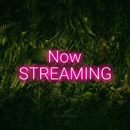 Hot pink LED neon sign reading "Now Streaming" against a moss-covered green wall for gaming room décor