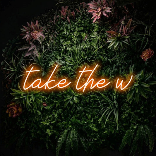 Orange script-style LED neon sign reading "Take the W" against a flowering garden wall for gaming room décor