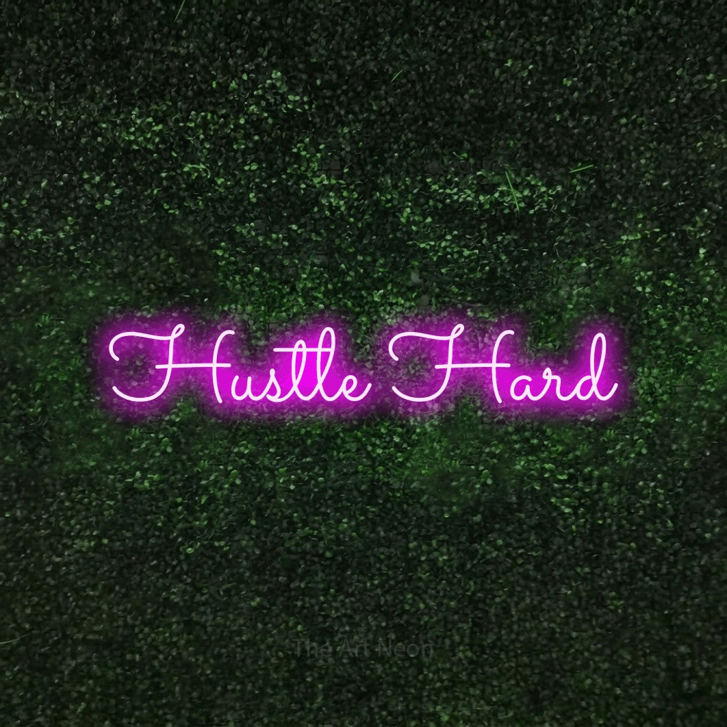 Pink LED neon sign reading "Hustle Hard" against a textured green moss wall