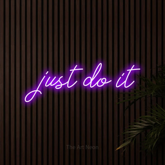 Purple script-style LED neon sign reading "Just Do It" against dark wooden slats