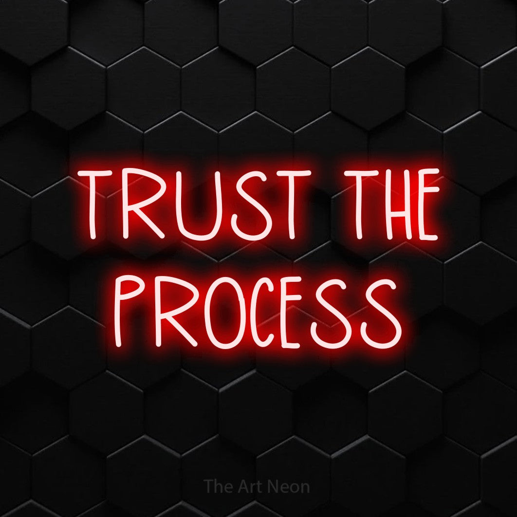 Red LED neon sign reading "Trust the Process" against a black hexagonal wall