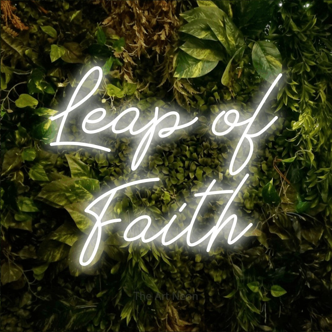 Cool white script-style LED neon sign reading "Leap of Faith" against a textured moss and foliage wall