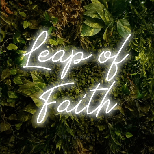 Cool white script-style LED neon sign reading "Leap of Faith" against a textured moss and foliage wall