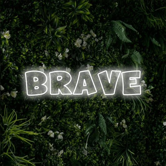Cool white outline-style LED neon sign reading "Brave" against a leafy green wall