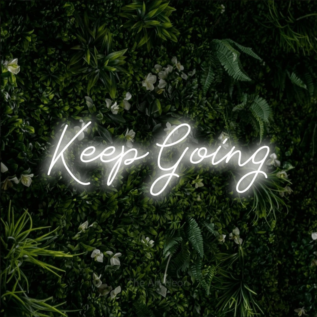 Cool white script-style LED neon sign reading "Keep Going" against a leafy green wall