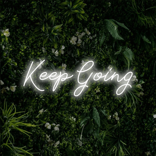 Cool white script-style LED neon sign reading "Keep Going" against a leafy green wall