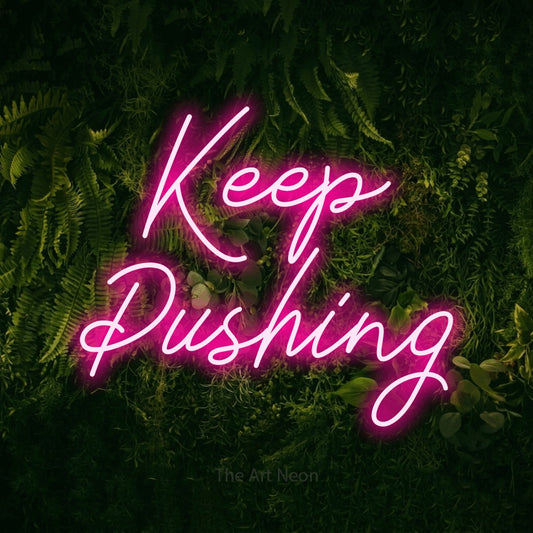 Hot pink script-style LED neon sign reading "Keep Pushing" against a moss-covered green wall
