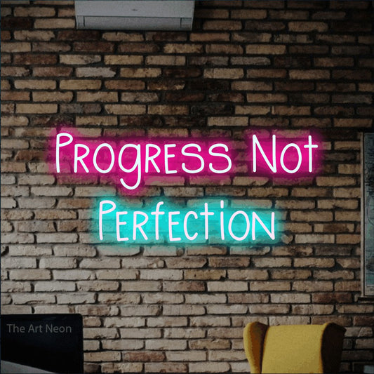 Ice blue and hot pink LED neon sign reading "Progress Not Perfection" against a rustic brick wall