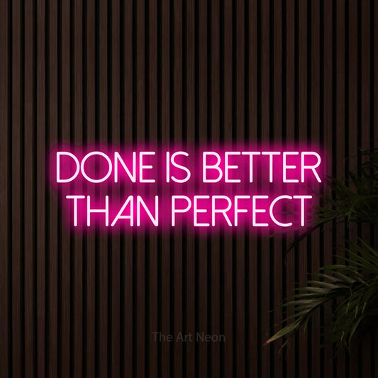 Hot pink LED neon sign reading "Done is Better Than Perfect" against dark wooden slats