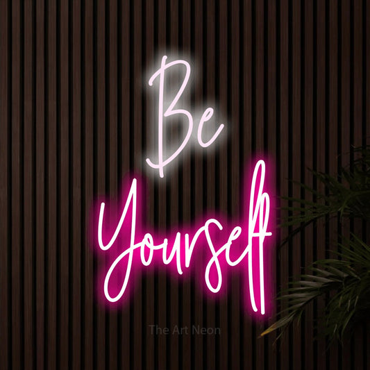 Hot pink and cool white script-style LED neon sign reading "Be Yourself" against dark wooden slats