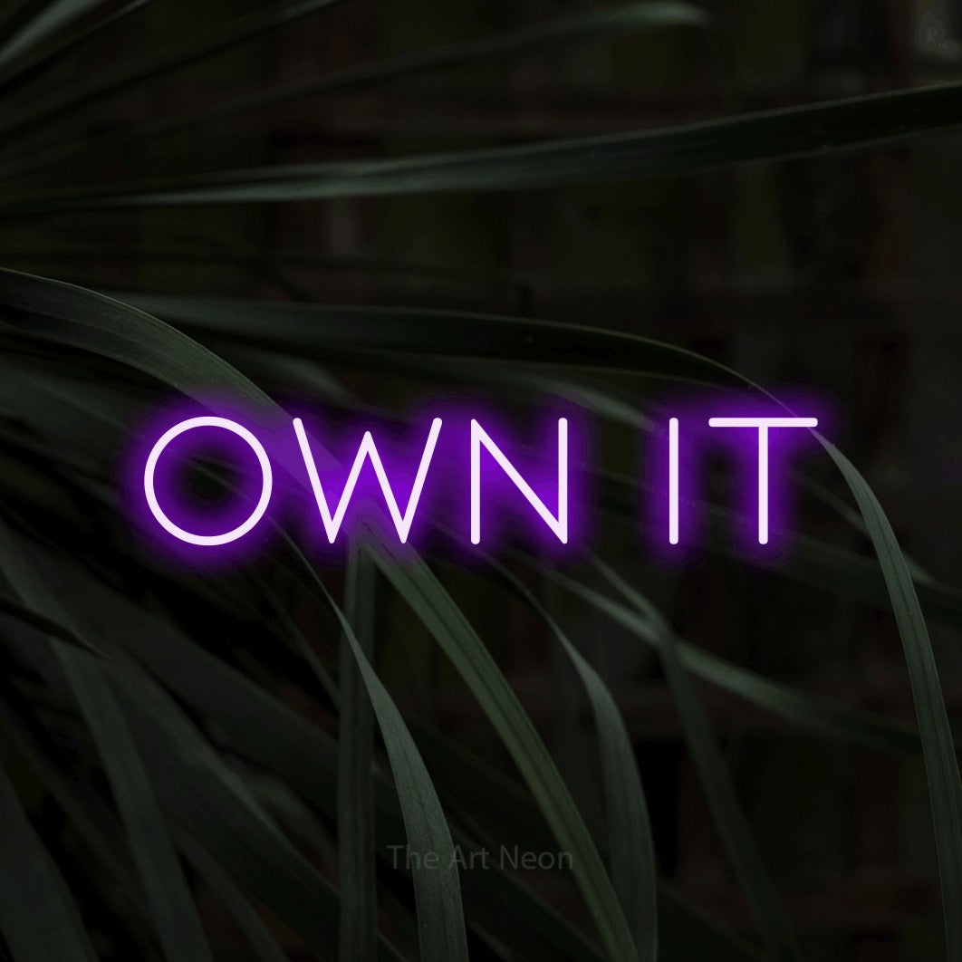 Purple LED neon sign reading "Own It" against dark tropical leaves