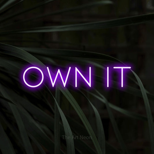 Purple LED neon sign reading "Own It" against dark tropical leaves
