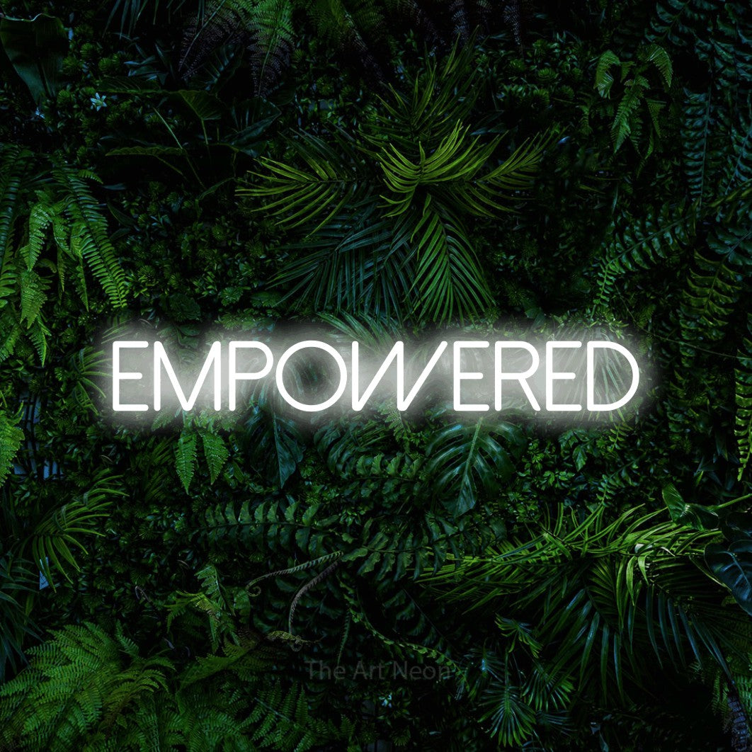 Cool white LED neon sign reading "Empowered" against a dense tropical foliage wall