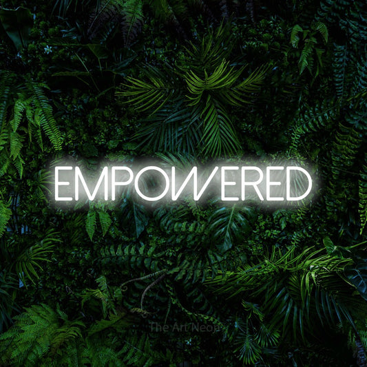 Enseigne néon à DEL à lumière blanche froide, affichant « Empowered » sur un mur de feuillage tropical dense
