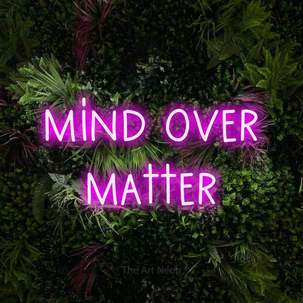 Pink LED neon sign reading "Mind Over Matter" against a lush garden wall with pink flowers