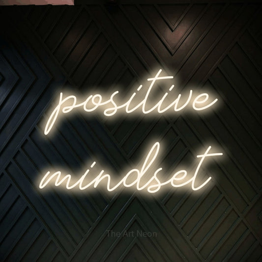 Enseigne néon à DEL à lumière blanche chaude, de style manuscrit, affichant « Positive Mindset » sur un mur géométrique en bois foncé