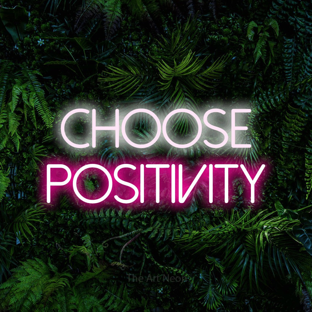 Hot pink and cool white LED neon sign reading "Choose Positivity" against a dense tropical foliage wall