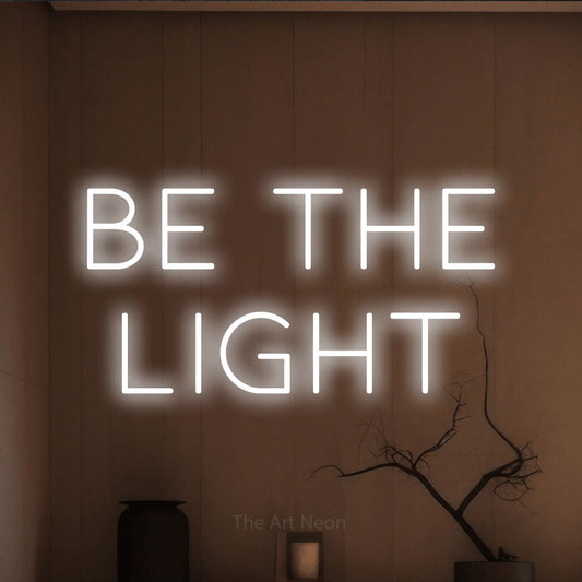 Enseigne néon à DEL à lumière blanche froide, affichant « Be the Light » sur un mur brun chaleureux