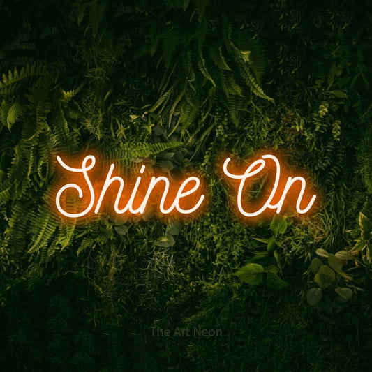 Enseigne néon à DEL à lumière orange, de style manuscrit, affichant « Shine On » sur un mur vert couvert de mousse