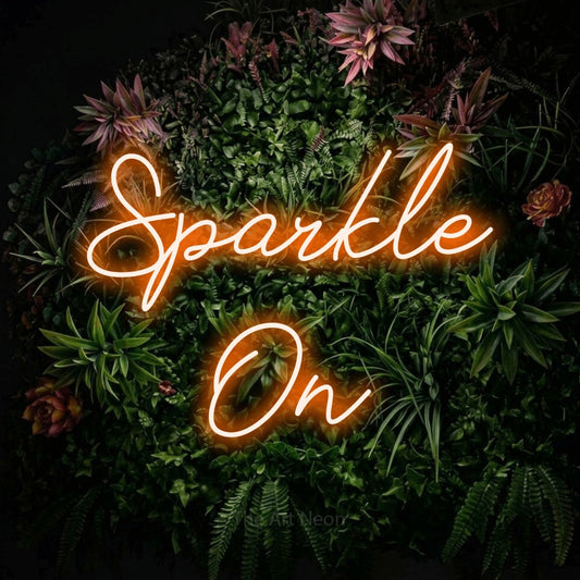 Enseigne néon à DEL à lumière orange, de style manuscrit, affichant « Sparkle On » sur un mur de jardin fleuri