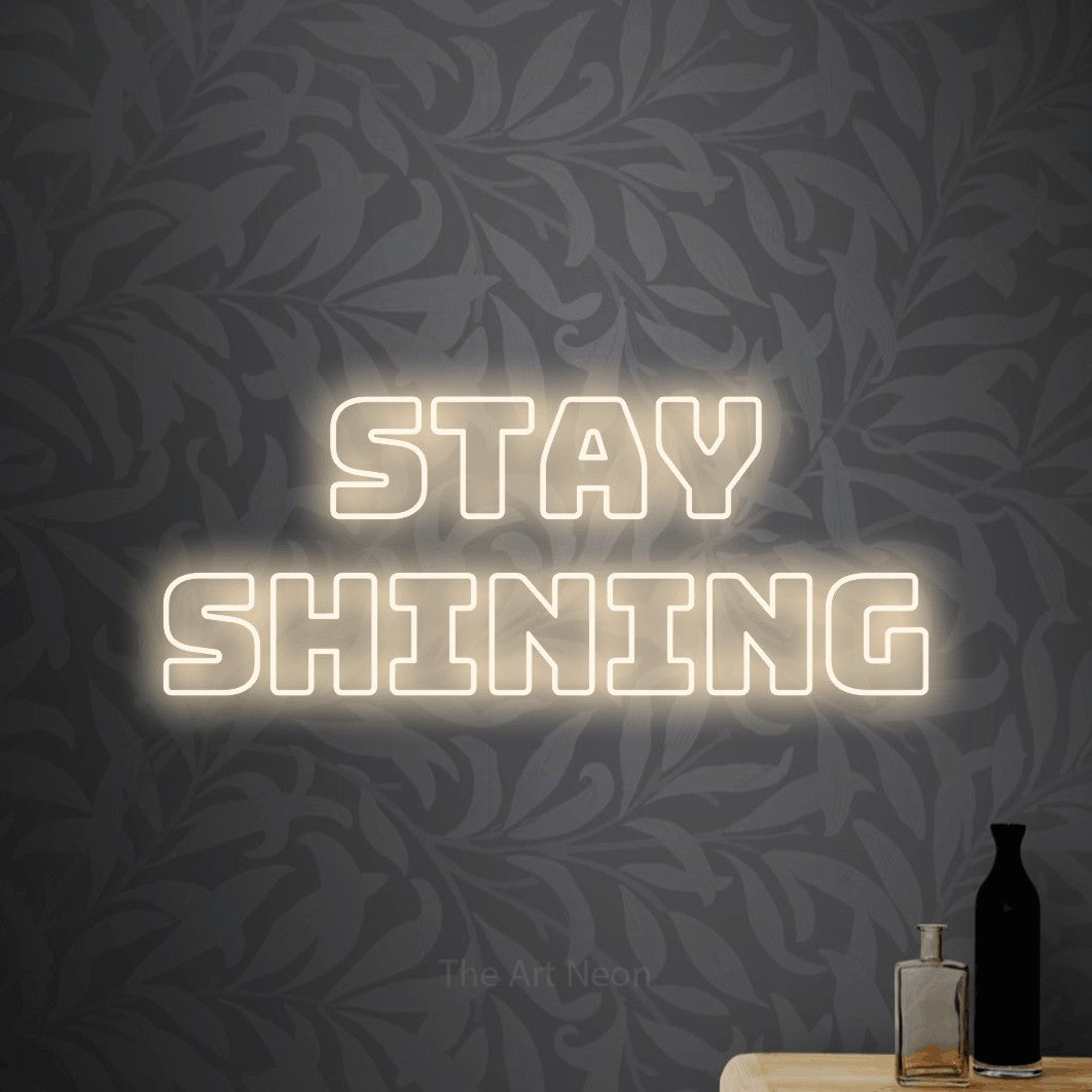 Warm white outline-style LED neon sign reading "Stay Shining" against light grey floral wallpaper