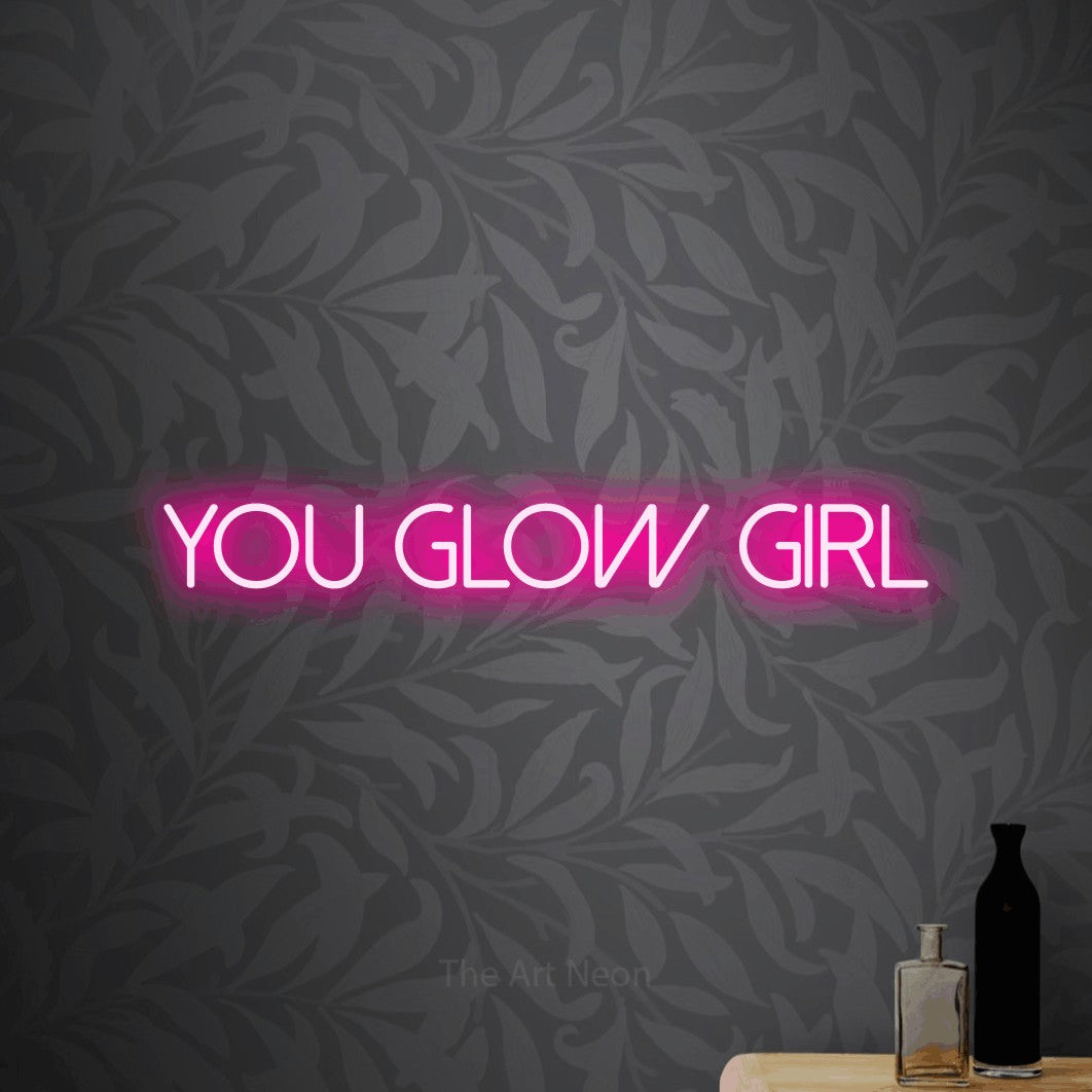 Hot pink LED neon sign reading "You Glow Girl" against light grey floral wallpaper