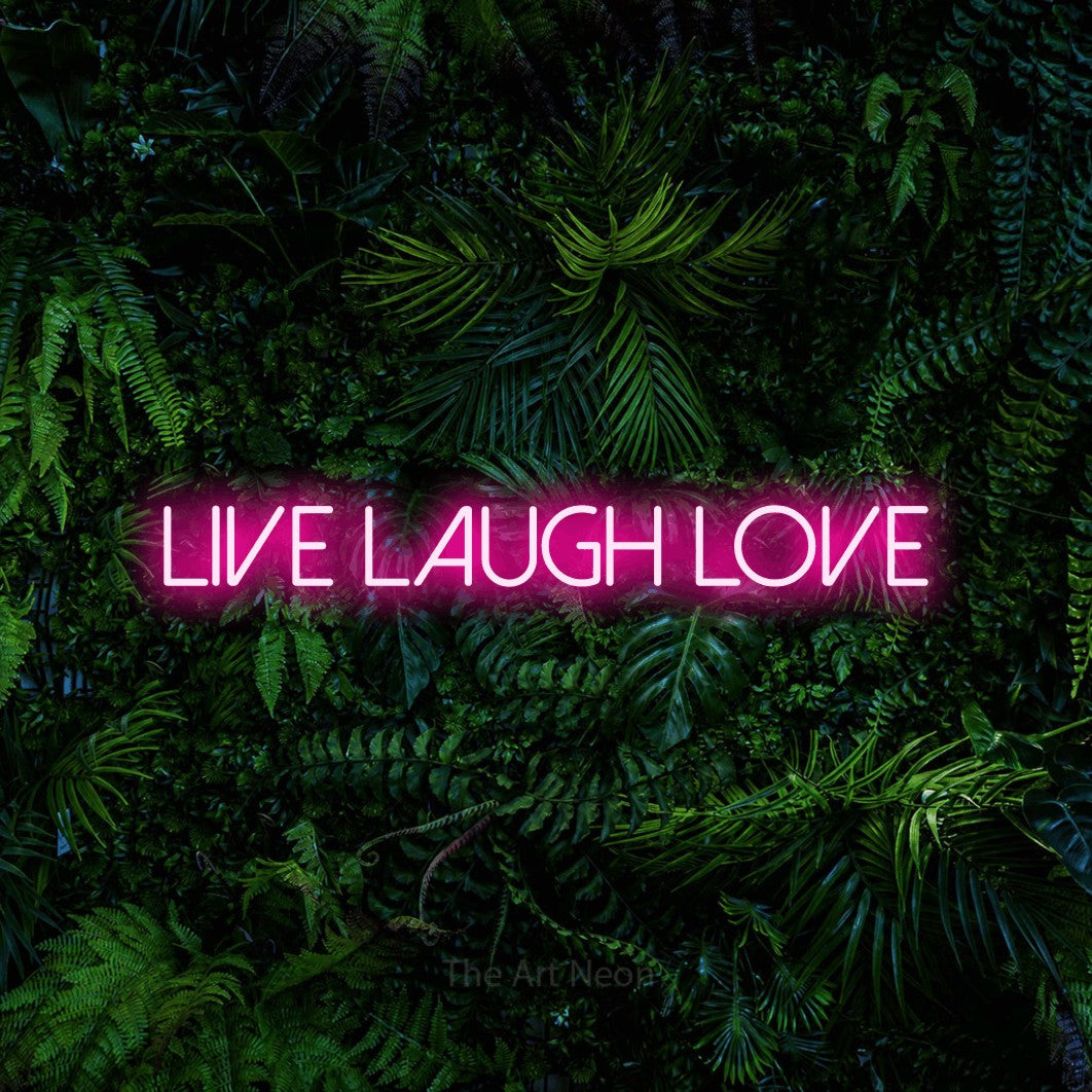 Hot pink LED neon sign reading "Live Laugh Love" against a dense tropical foliage wall