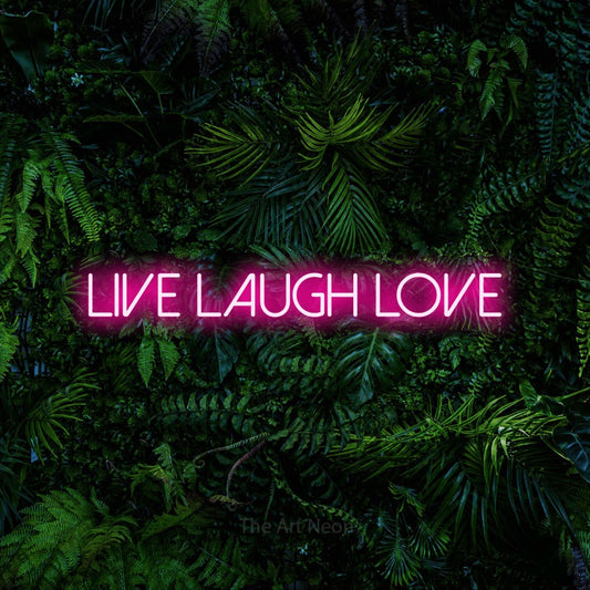 Hot pink LED neon sign reading "Live Laugh Love" against a dense tropical foliage wall