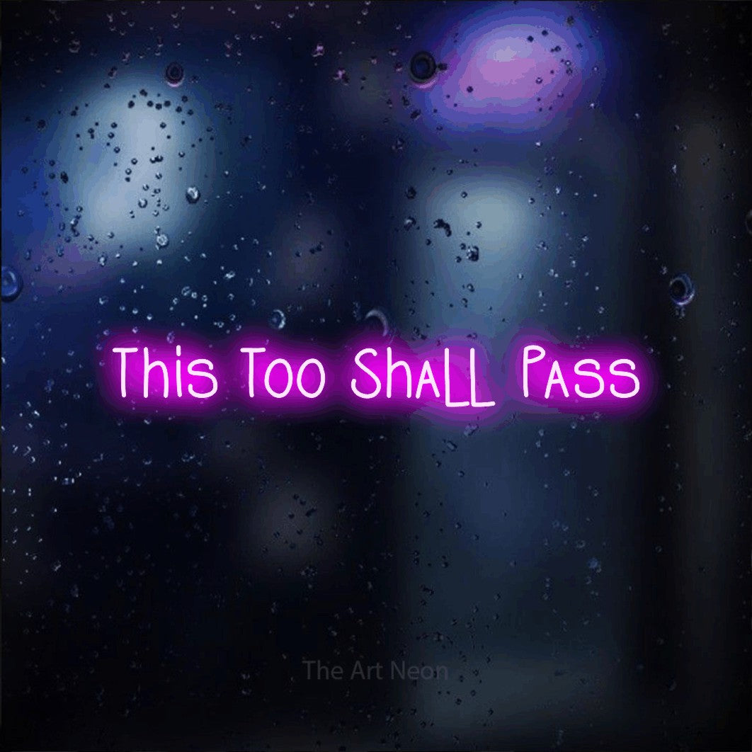 Pink LED neon sign reading "This Too Shall Pass" against a dark blue bokeh background