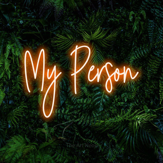 Orange script-style LED neon sign reading "My Person" against a dense tropical foliage wall