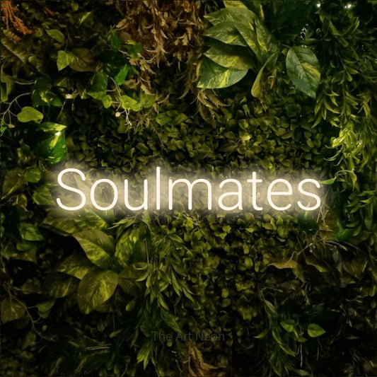Warm white LED neon sign reading "Soulmates" against a textured moss and foliage wall