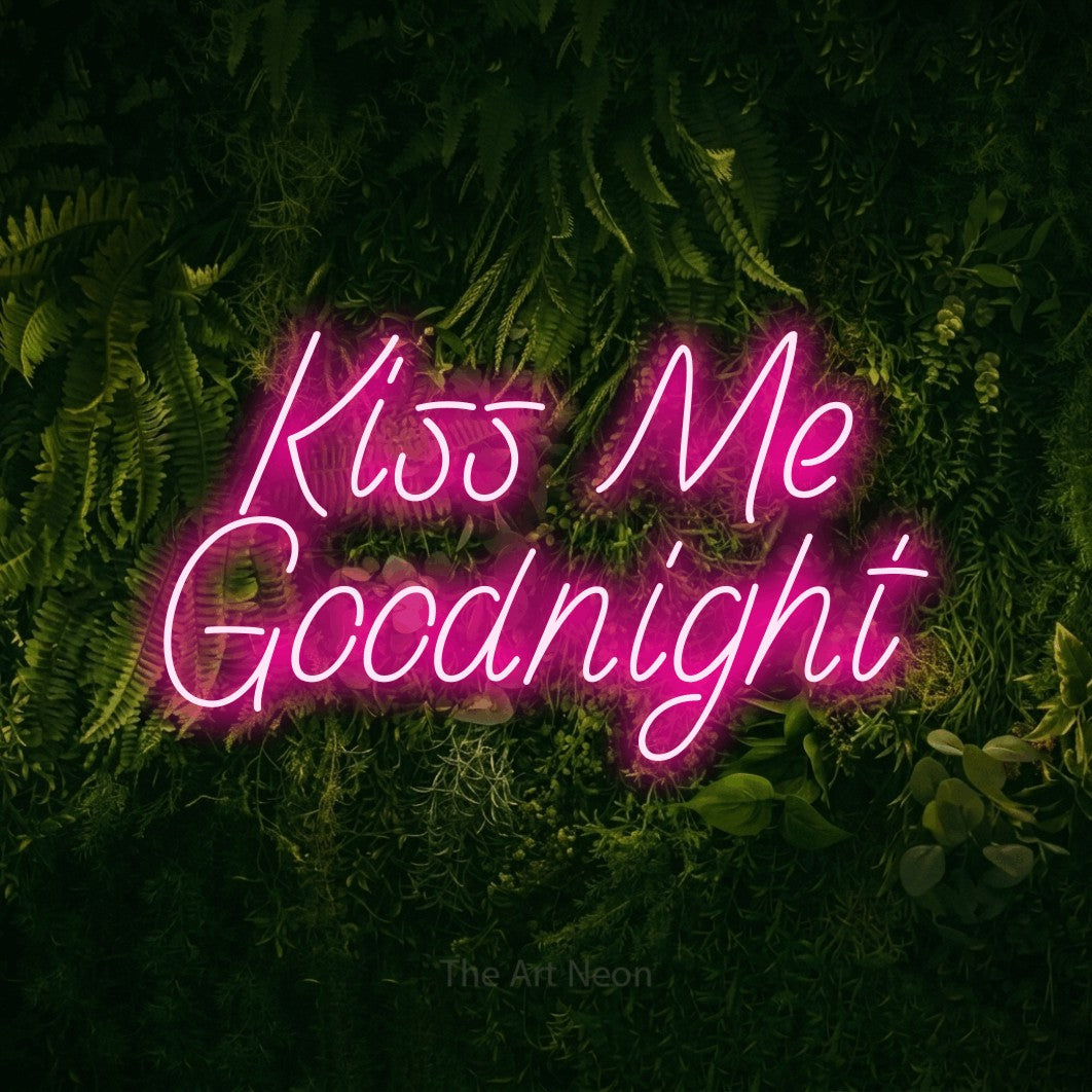 Hot pink LED neon sign reading "Kiss Me Goodnight" against a moss-covered green wall