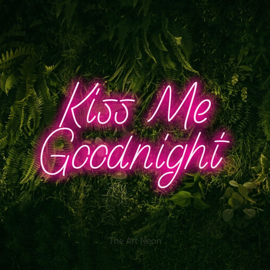 Hot pink LED neon sign reading "Kiss Me Goodnight" against a moss-covered green wall