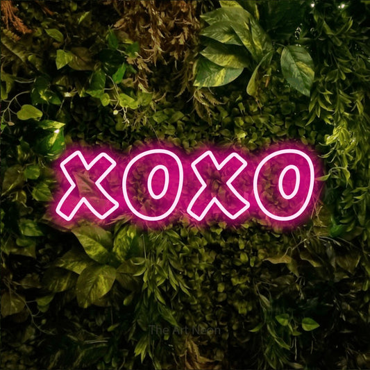 Hot pink outline-style LED neon sign reading "XOXO" against a textured moss and foliage wall