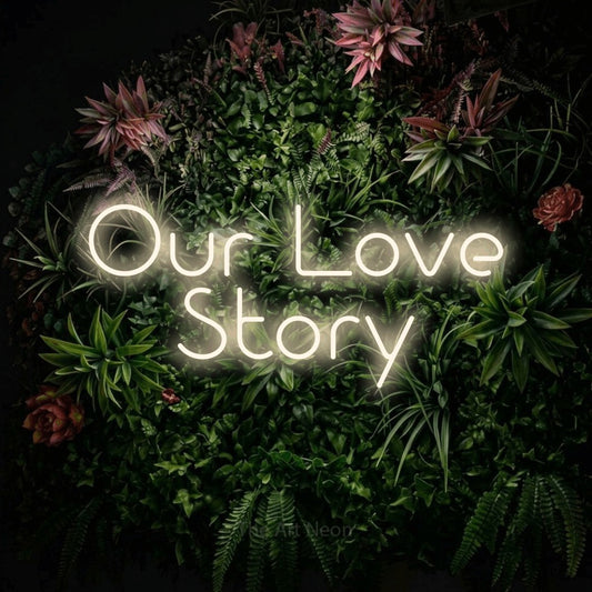 Warm white LED neon sign reading "Our Love Story" against a flowering garden wall