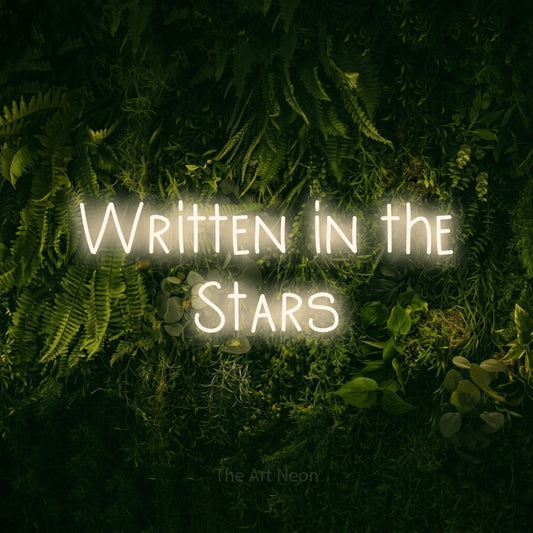 Warm white LED neon sign reading "Written in the Stars" against a moss-covered green wall