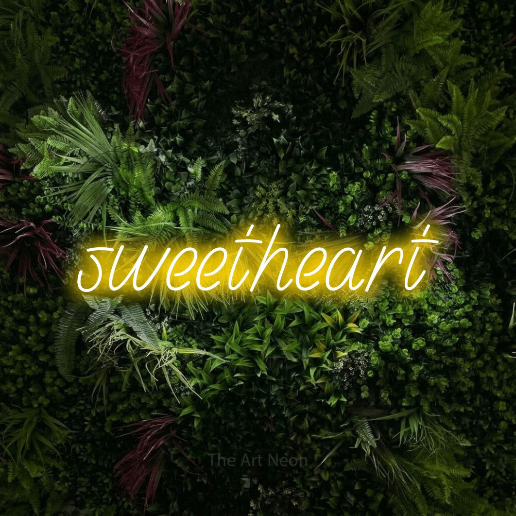 Enseigne néon à DEL à lumière jaune, affichant « Sweetheart » sur un mur de jardin luxuriant aux fleurs roses