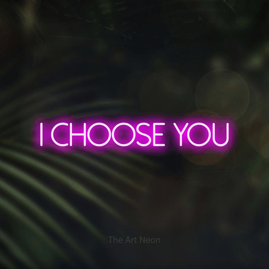 Pink LED neon sign reading "I Choose You" against dark blurred palm leaves