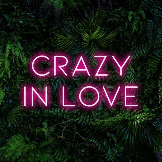 Hot pink LED neon sign reading "Crazy in Love" against a dense tropical foliage wall