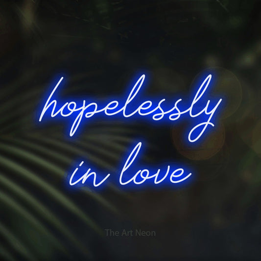 Blue script-style LED neon sign reading "Hopelessly in Love" against dark blurred palm leaves
