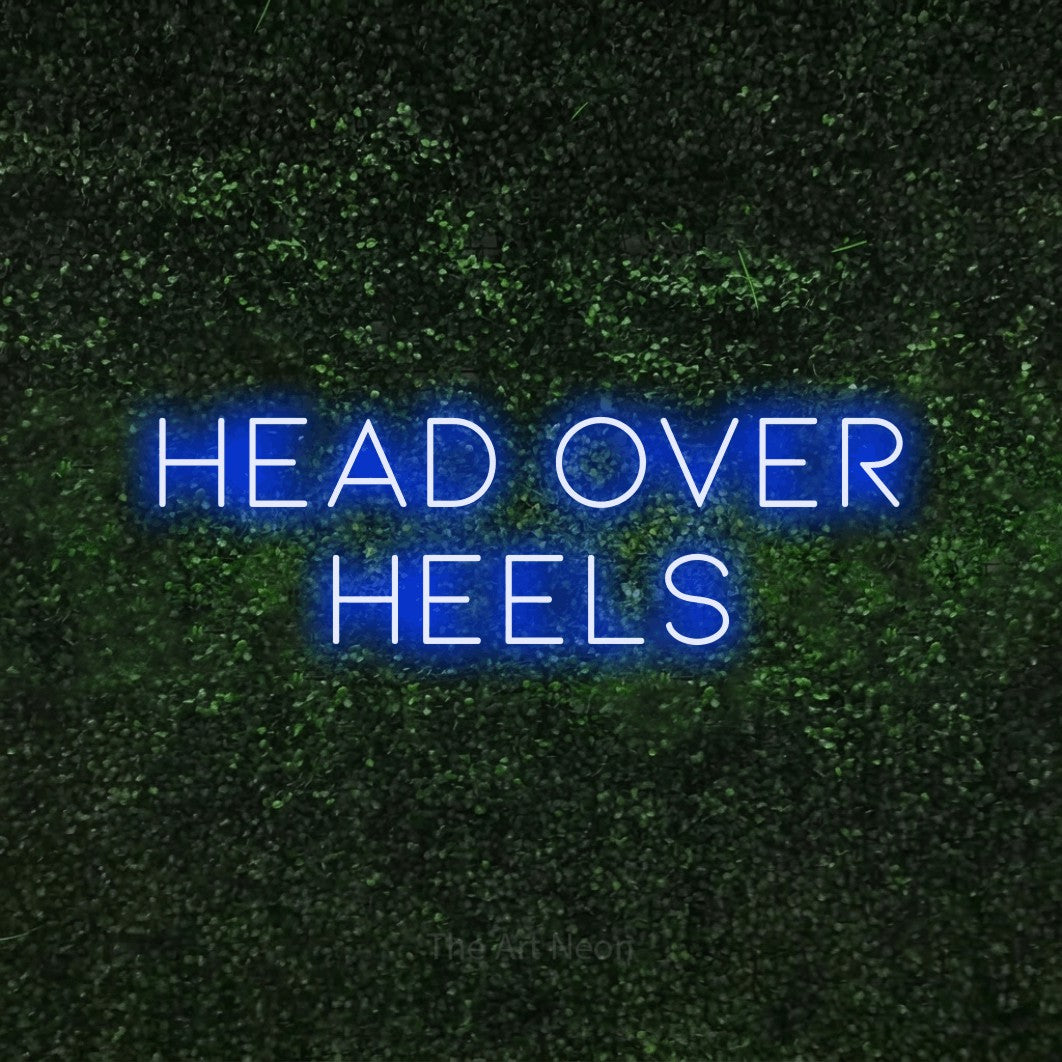 Blue LED neon sign reading "Head Over Heels" against a textured green moss wall