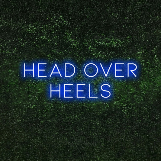 Blue LED neon sign reading "Head Over Heels" against a textured green moss wall