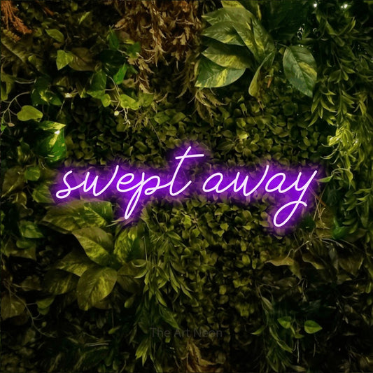 Purple script-style LED neon sign reading "Swept Away" against a textured moss and foliage wall