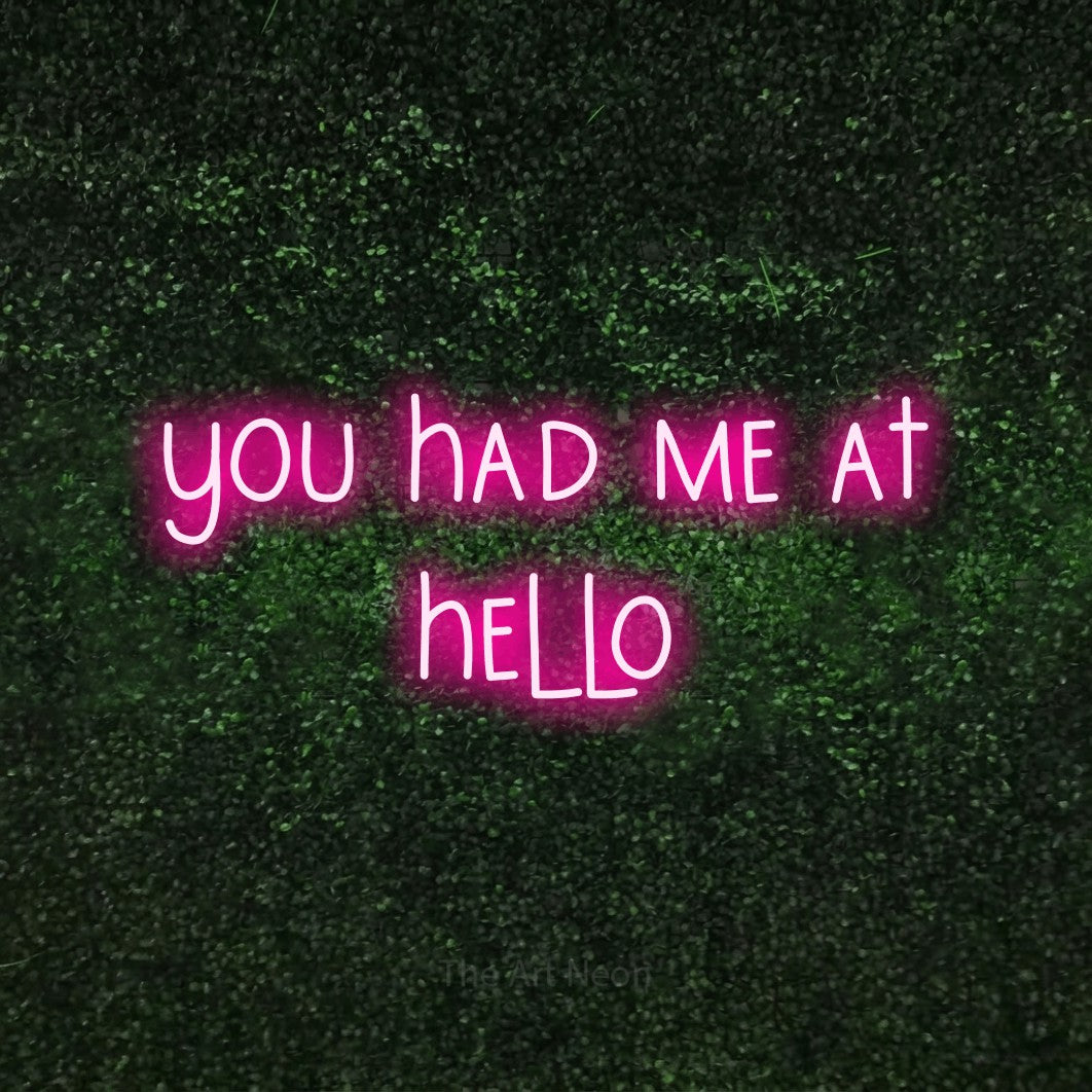 Hot pink LED neon sign reading "You Had Me at Hello" against a textured green moss wall