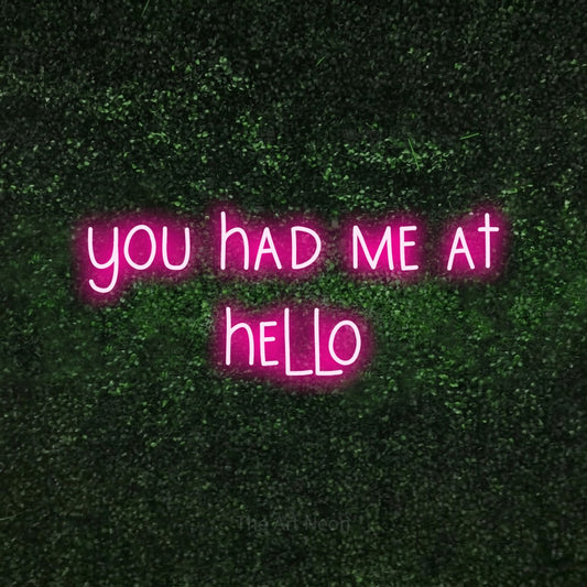 Hot pink LED neon sign reading "You Had Me at Hello" against a textured green moss wall