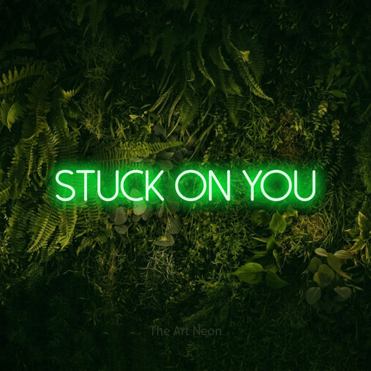 Green LED neon sign reading "Stuck on You" against a moss-covered green wall